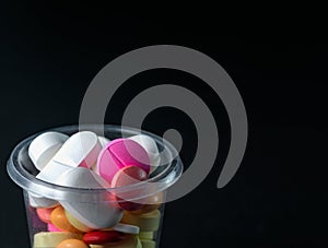 Closeup shot of pharmaceuticals pills and antibiotics in a plastic cup on a black background