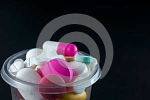 Closeup shot of pharmaceuticals pills and antibiotics in a plastic cup on a black background