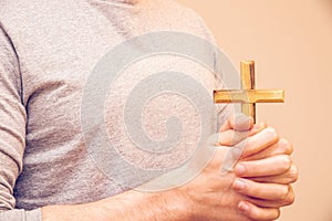 Closeup shot of a praying man with a cross on his hands