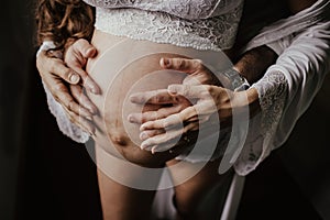 Closeup shot of a pregnant woman`s exposed abdomen with a man`s hands holding abdomen from behind