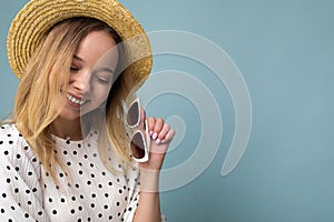 Closeup shot of pretty positive smiling young blonde woman wearing summer dress straw hat and stylish sunglasses