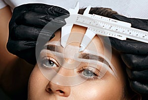 Cosmetician measuring brows before permanent makeup procedure photo