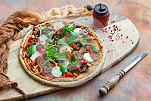 Closeup shot of raw vegan pizza next to an old pepper mill with dried peppercorns on a wooden board