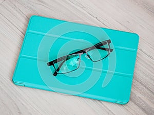 Closeup shot of reading glasses with light blue leather folio case for tablet