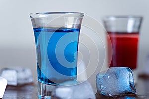 Closeup shot of red and blue cocktail shots  and melting ice cubes on  a wooden table