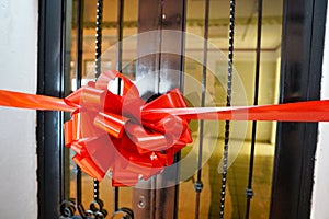 Closeup shot of a red ribbon with a bow in front of a wooden door with glass windows