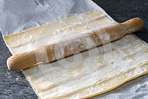 Closeup shot of a rolling pin on top of a square dough with flour