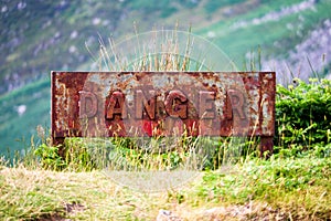 Closeup shot of a rusty old danger sign on a mountainside