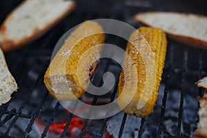 Closeup shot of salted corn grilled next to bread on the grates outdoors