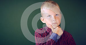 Closeup shot of schoolboy thinking with hand on chin isolated on blackboard. Portrait of pensive child thinking about