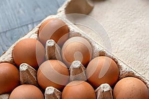 Closeup shot of set of brown chicken eggs in a recycled cardboard box. Box with eggs is on the grey wooden surface in the kitchen