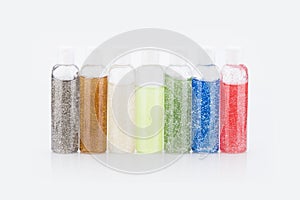 Closeup shot of seven bottles of colorful glitter on a white background