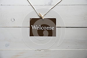 Closeup shot of a sign with welcome written on it and a white wooden background