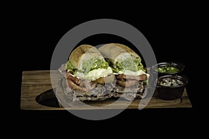 Closeup shot of a sliced ham sandwich with sauces on a wooden desk with a black background