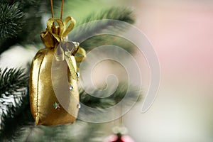 Closeup shot of small lovely seasonal festival decorative bright shiny golden bag hanging on Christmas green pine tree on x-mas