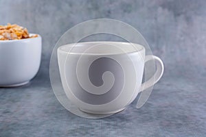 Closeup shot of a small white mug isolated and a bowl of cereal on a gray background