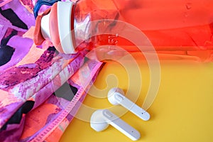 Closeup shot of sportswear, wireless earphones and a plastic water bottle on a yellow surface