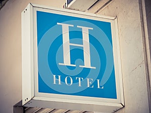 Closeup shot of a square blue sign with a large letter H and the word Hotel under it in white