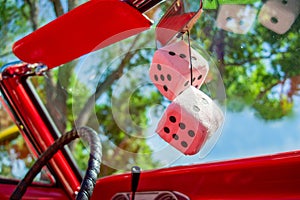 Closeup shot of a steering wheel and white decorative dices in the red retro car