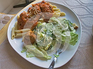 Closeup shot of tasty pasta with tomato meat sauce and fresh caesar salad on a white plate