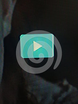 Closeup shot of a teal play button on a screen, showcasing the pixelated texture. Ideal for tech, digital media, and videorelated