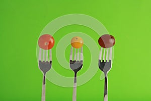 Closeup shot of three colorful cherry tomatoes on forks with a green background