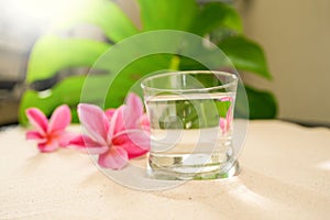 Closeup shot of a transparent glass full of water against the background of pink plumerias