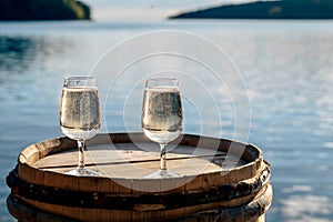 Closeup shot of two full wineglasses on the top of a wooden barrel against a blue sea