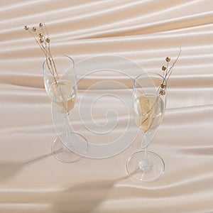 Closeup shot of two glasses of champagne with golden pearls on beige claoth
