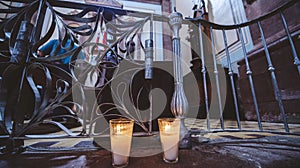 Closeup shot of two lit candles near a metal fence in the church with a blurred background