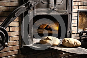 Closeup shot of two loaves of freshly baked bread being taken out of an old masonry brick oven