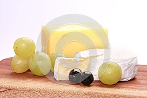 Closeup shot of two types of cheese and grapes on a chopping board isolated on a white background