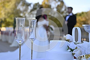 Closeup shot of two wedding champagne flutes on an outdoor table with a couple in the background