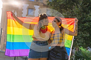 Closeup shot of two young Caucasian females holding LGBT pride flag outdoors