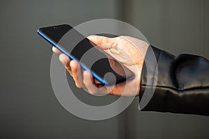 Closeup shot of an unrecognizable young man holding mobile phone in hand, blurred background