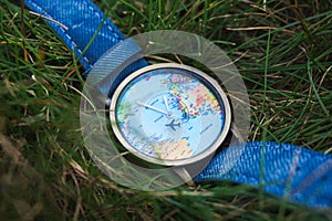 Closeup shot of a watch with a design of the world map on the grassy terrain