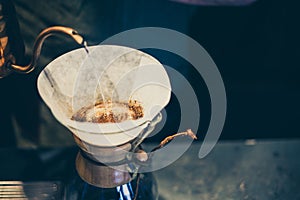 Closeup shot of water pouring into a coffee filter with ground bits over a glass pot