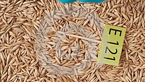 Closeup shot of wheat grains background, hand in glove puts paper sign with E 121 written on it.