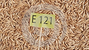 Closeup shot of wheat grains background, person puts paper sign with E 121 written on it.