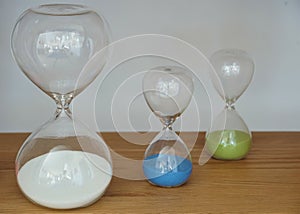 Closeup shot of white, blue, and green hourglasses on a wooden surface