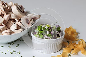 Closeup shot of a white bowl of a vegetable salad and a bowl of sliced mushrooms