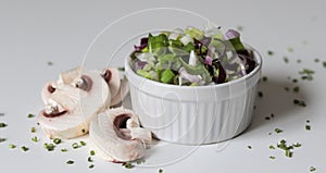 Closeup shot of a white bowl of a vegetable salad and sliced mushrooms on a white surface