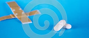 Closeup shot of white pills and a medical patch isolated on an empty blue background