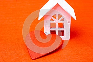 Closeup shot of a white wooden house and a red heart on an orange surface