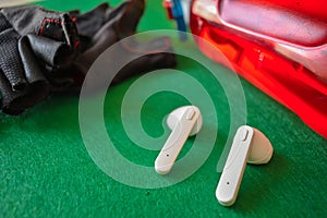Closeup shot of wireless earphones, gym gloves and a plastic water bottle on a green surface