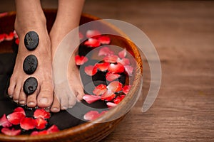 Closeup shot of a woman feet dipped in water with petals in a wooden bowl