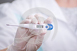 Closeup shot of a woman looking at thermometer. Female hands holding a digital thermometer. Girl measures the temperature. Shallow