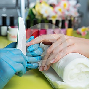 Closeup shot of a woman in a nail salon receiving a manicure by a beautician with nail file. Woman getting nail manicure