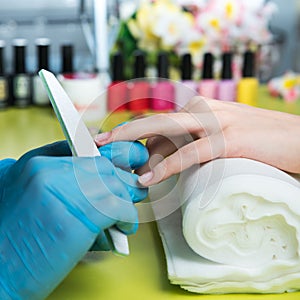 Closeup shot of a woman in a nail salon receiving a manicure by a beautician with nail file. Woman getting nail manicure. Beautici