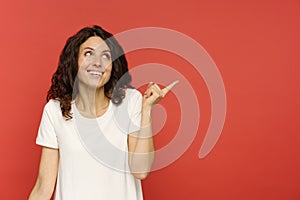 Closeup shot of woman with pleasured smile point finger side to copy space on red studio background